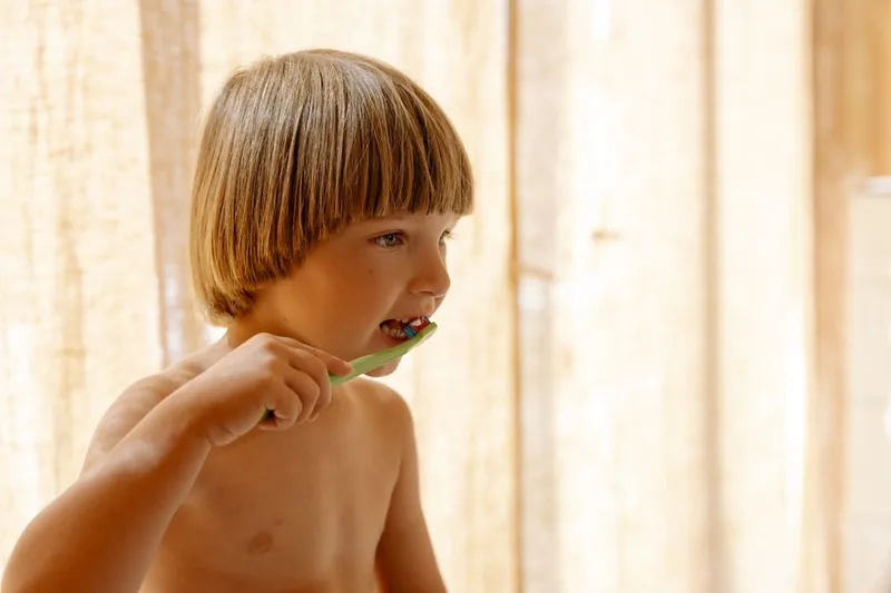 Illustrative photo of a young child brushing their teeth in soft daylight