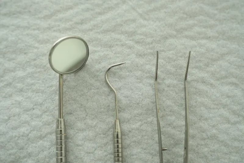 Illustrative close-up of a dental mirror, probe and tweezers laid out on a clean cloth