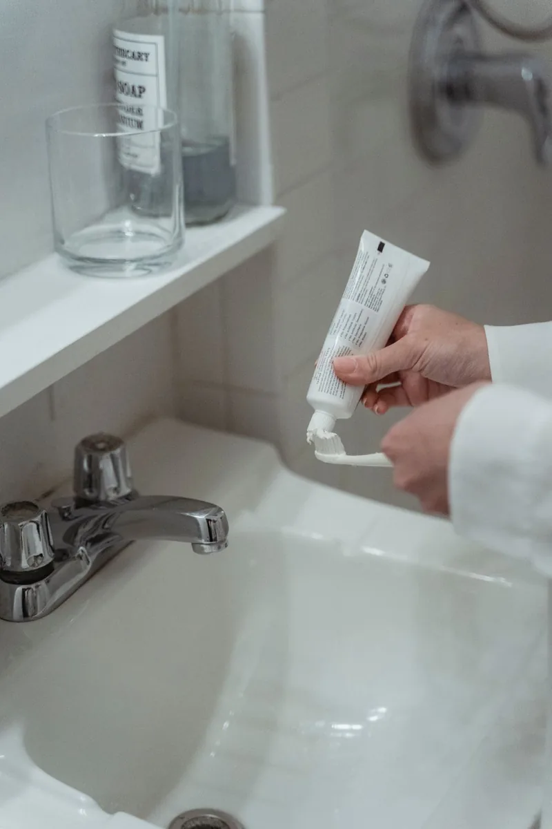 Illustrative photo of toothpaste being squeezed onto a toothbrush at a clean bathroom basin