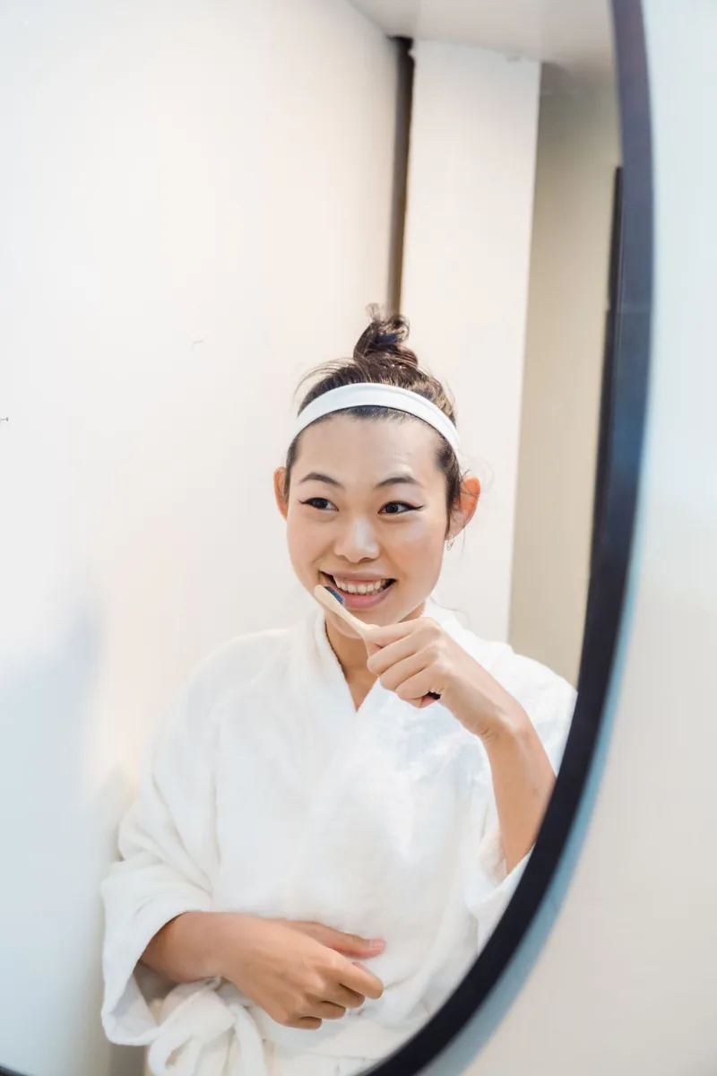 Illustrative photo of a woman brushing her teeth in front of a bathroom mirror